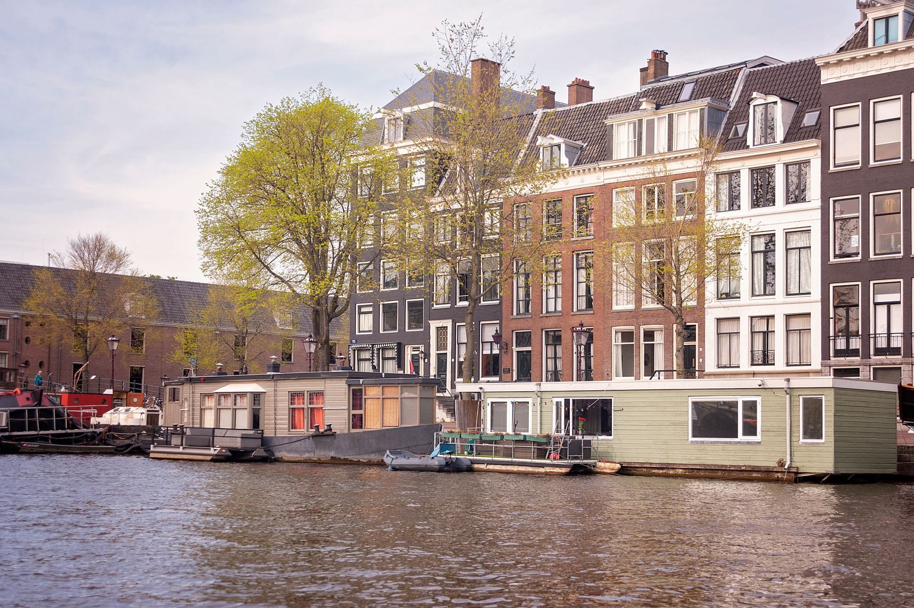 Kanał w Amsterdamie z barkami mieszkalnymi i zabytkowymi kamienicami